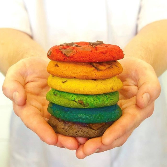 A chef holds a stack of colorful rainbow chocolate chip cookies.